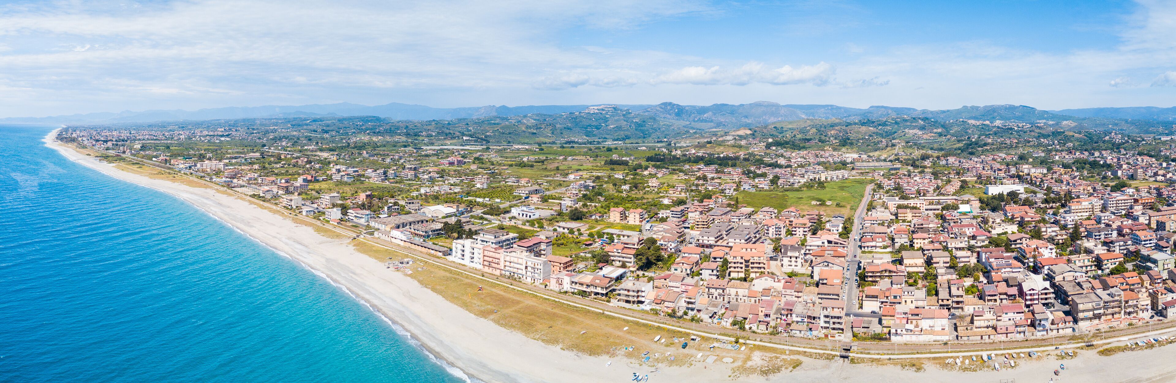 A coastal city with a beach, residential areas, and rolling hills in the background.