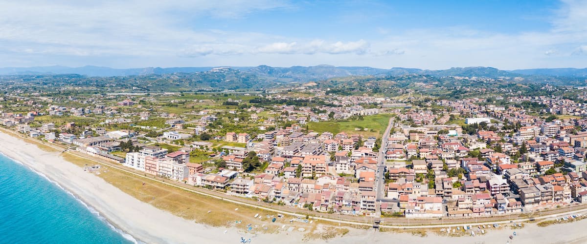 A coastal city with a beach, residential areas, and rolling hills in the background.