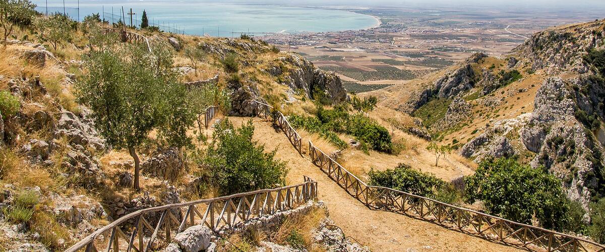A mountainous landscape with a dirt path leading to a coastal view.