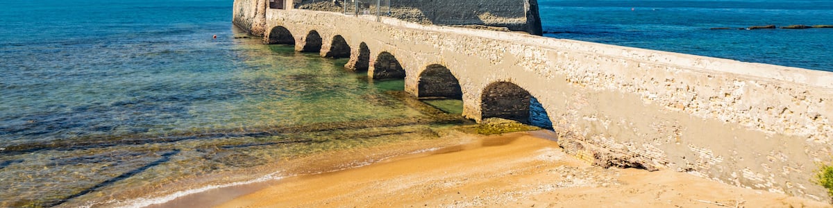 A coastal fortress with a tower, a bridge leading to it, and the sea in the background.