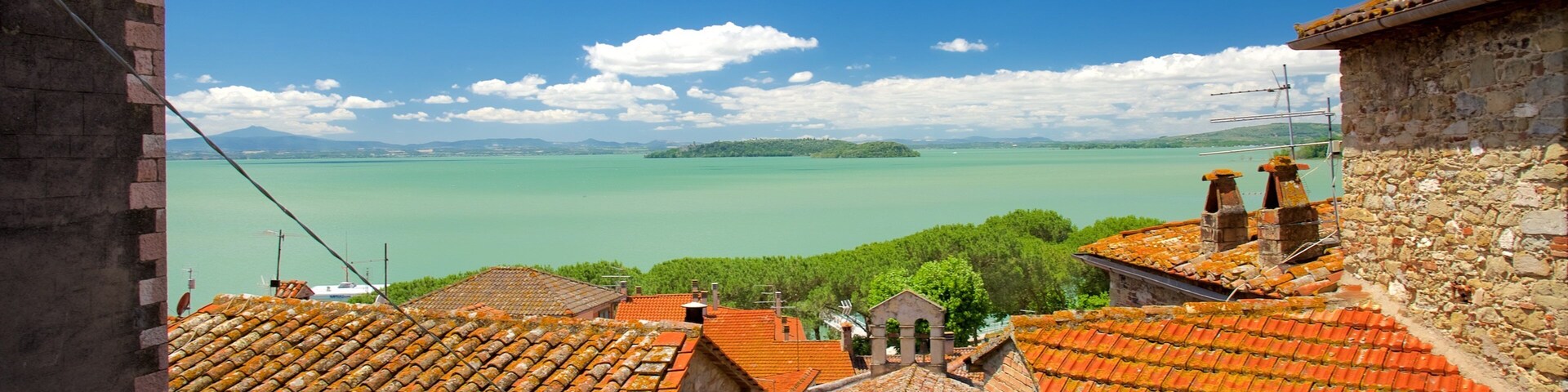 Uma vila costeira com telhados de terracota, céu azul límpido e mar calmo.