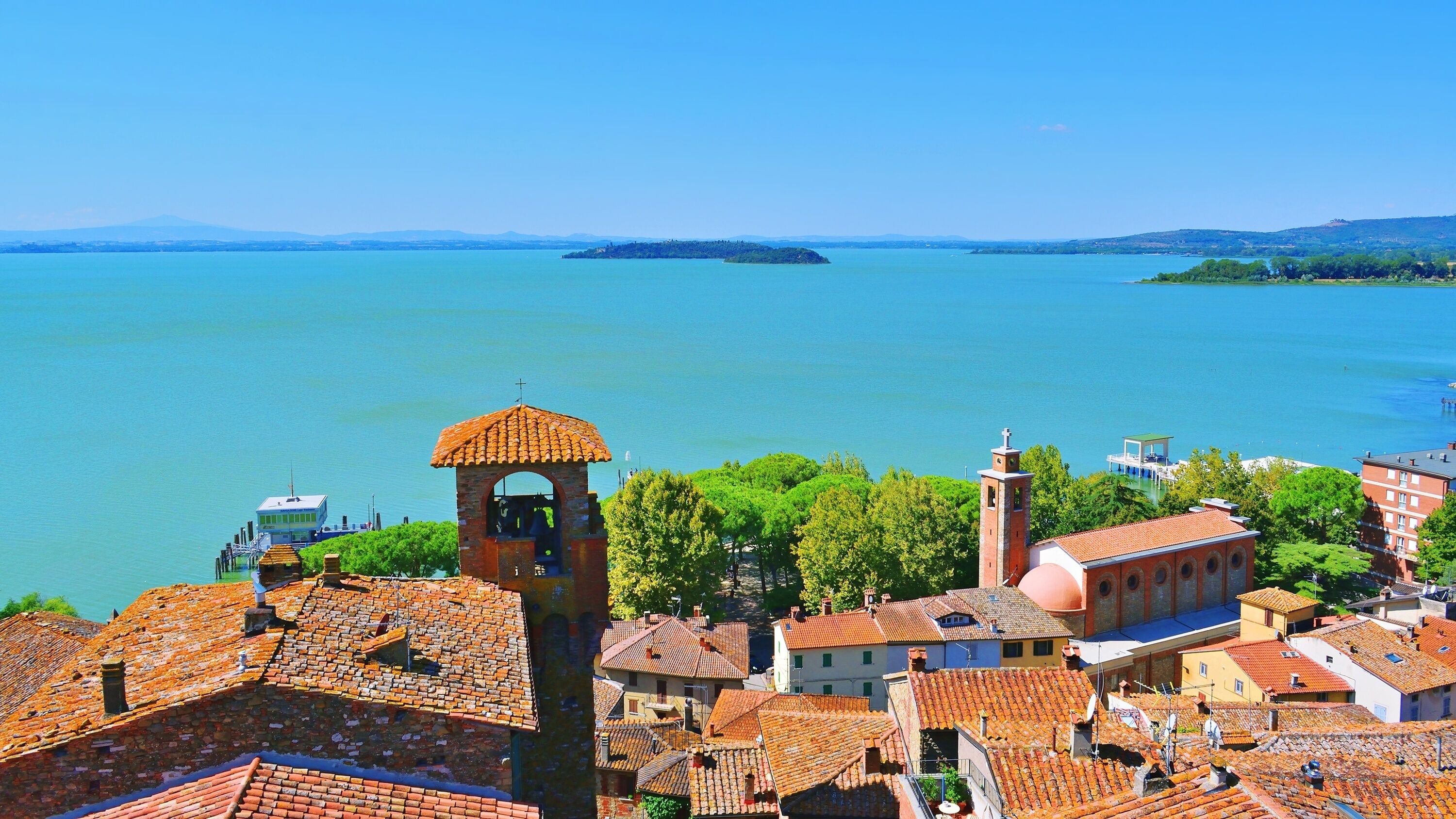 Un pueblo costero con edificios de tejados terracota, una torre de campanas y una vista despejada del mar.