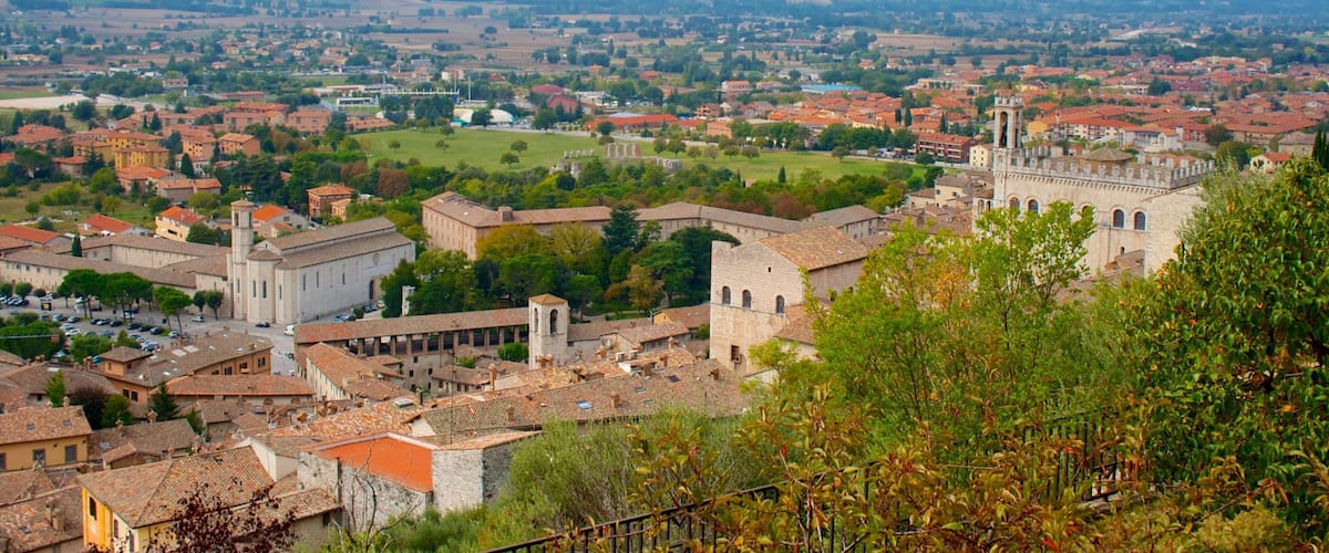 A panoramic view of a historic town with red-roofed buildings, a prominent church, and rolling hills in the background.