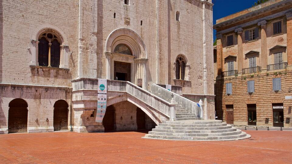 A historic building with a central staircase, arched windows, and a red brick plaza.