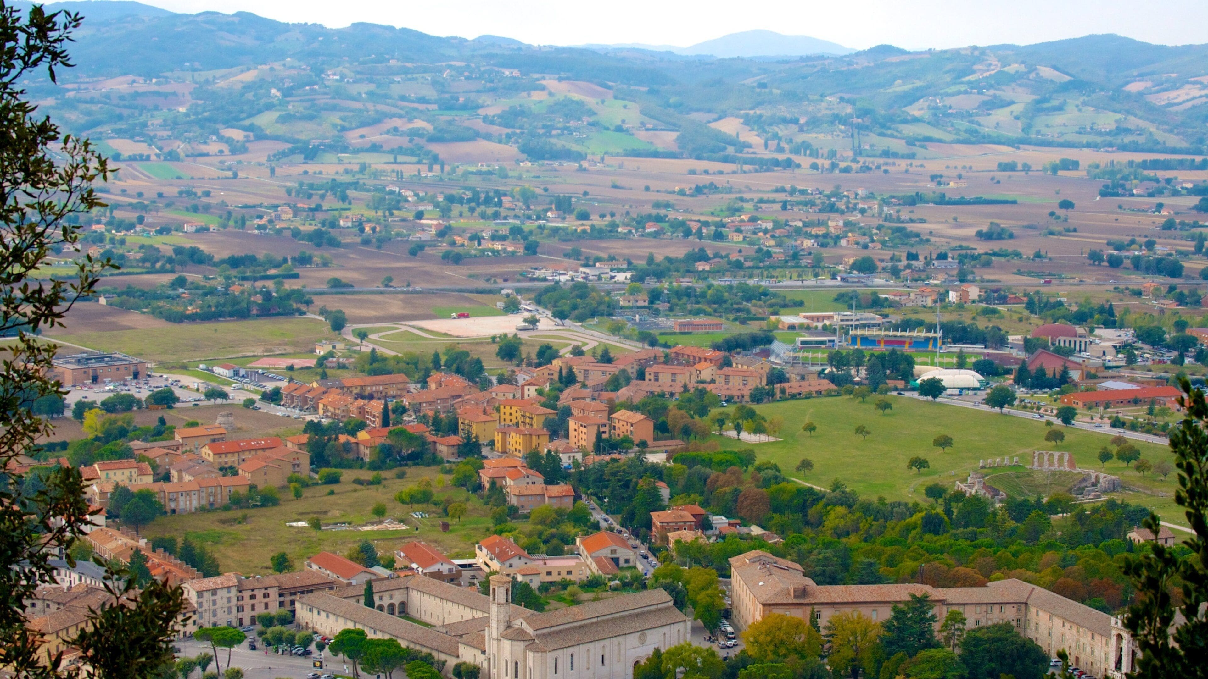 A town with historic architecture, green fields, and rolling hills in the background.