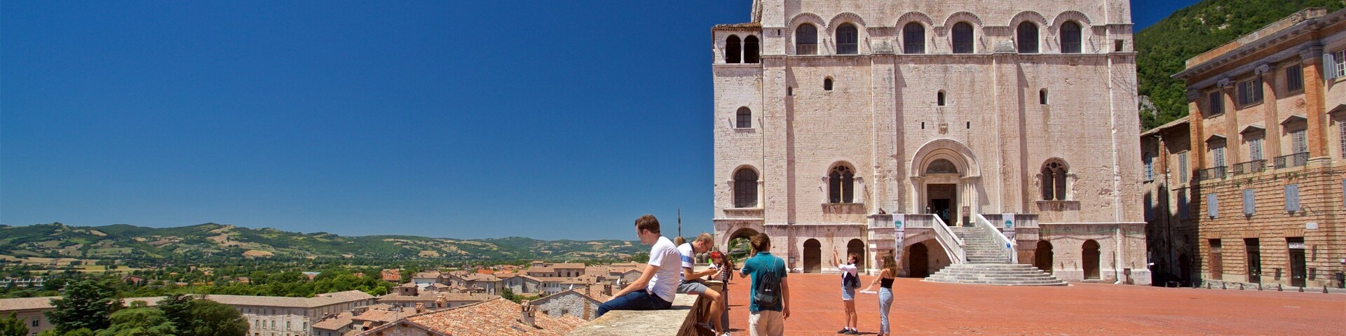Un edificio histórico con una torre de campanas, techo de tejas rojas y vistas del paisaje circundante.