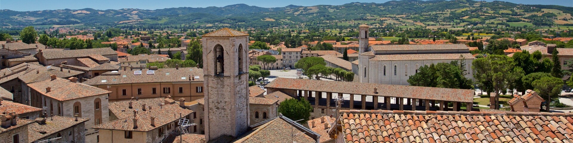Un pueblo histórico con edificios de tejas color terracota, una torre de iglesia destacada y colinas ondulantes al fondo.
