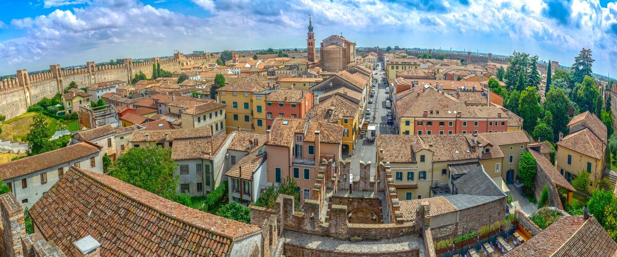 A panoramic view of a historic city with a prominent fortification, a central church, and a dense arrangement of terracotta-roofed buildings.