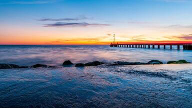 A sunset over a calm sea with a pier extending into the water.