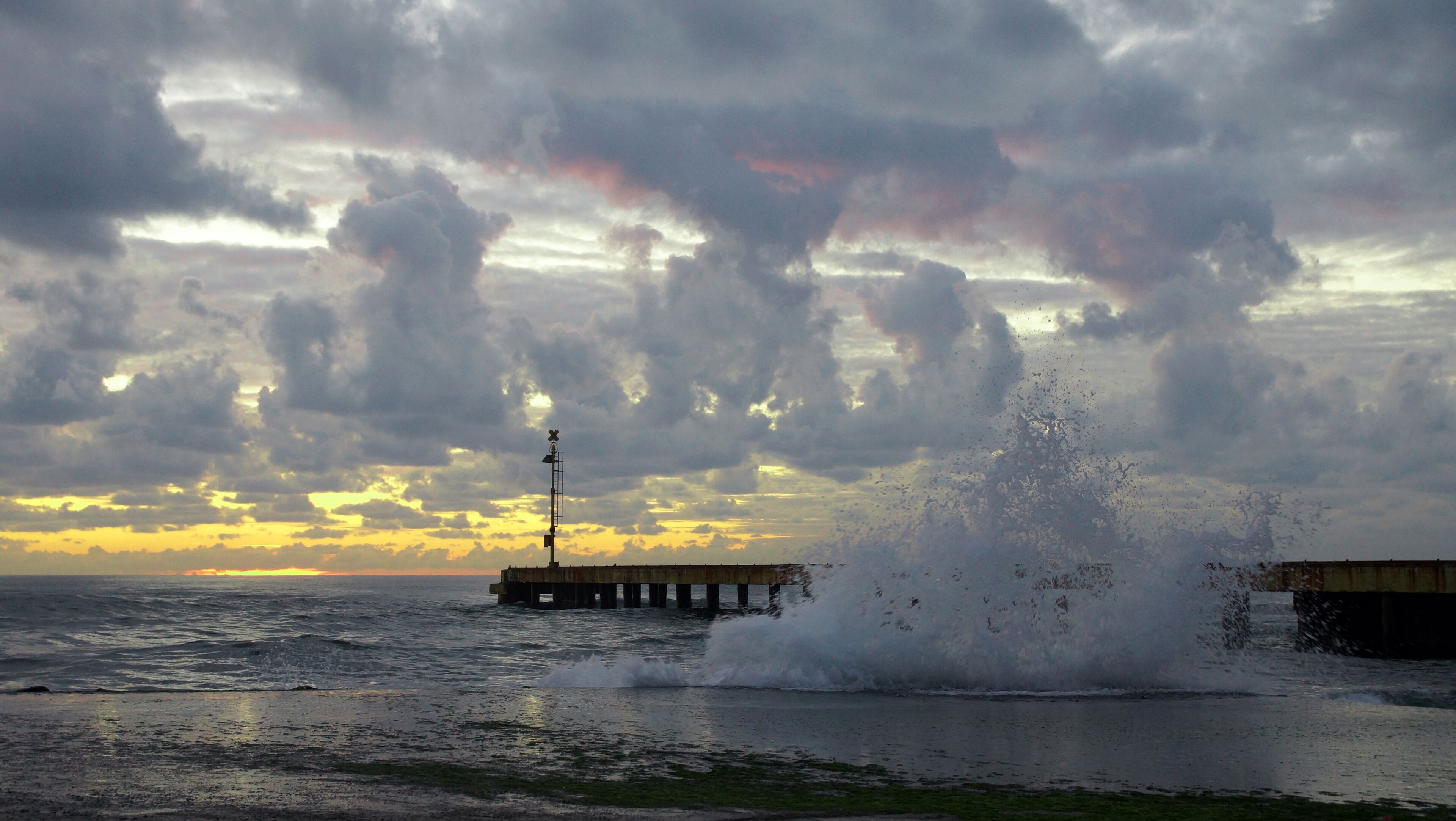 A pier extending into the ocean with waves crashing against it.