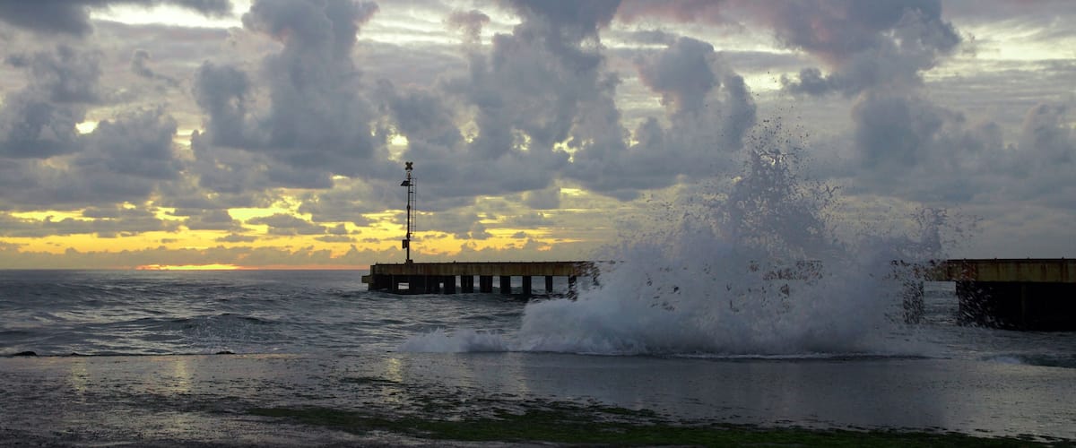 A pier extending into the ocean with waves crashing against it.