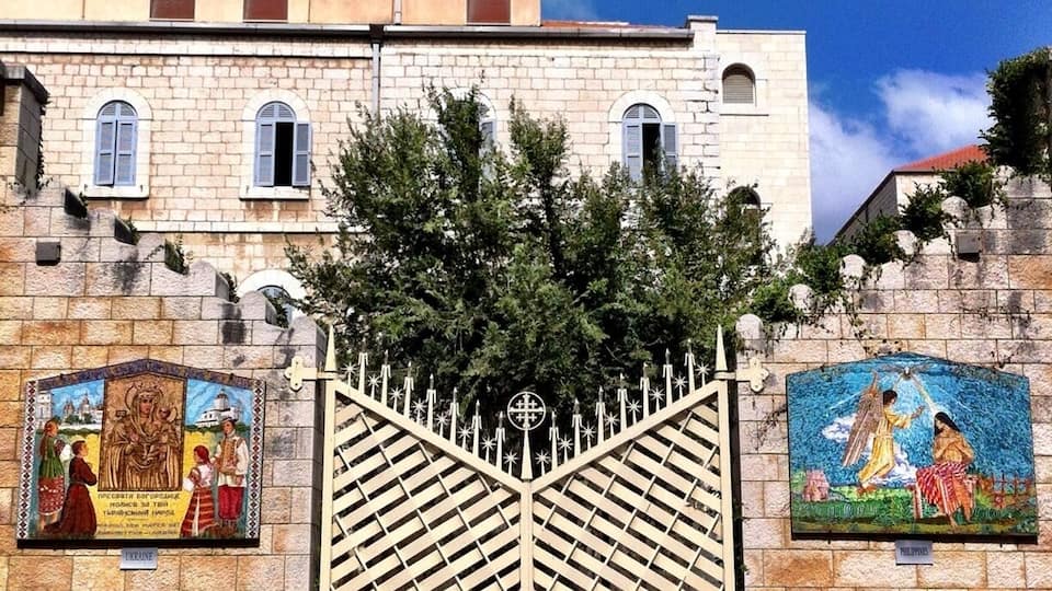 A building with a gate, mosaic artwork, and a tree.