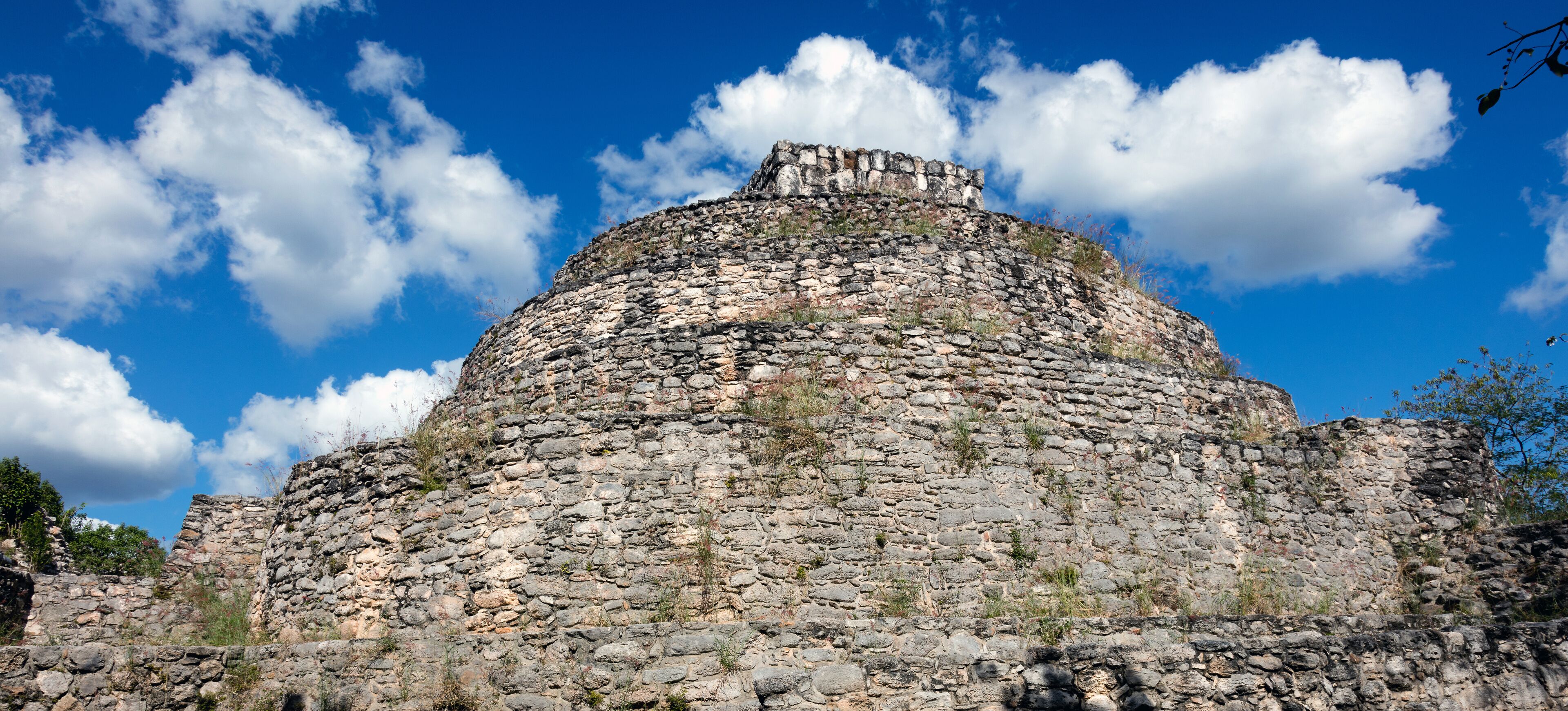 A stone pyramid with a flat top, surrounded by a clear blue sky and some clouds.