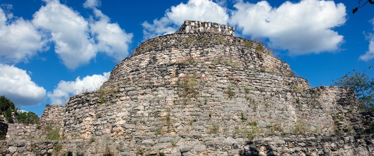 A stone pyramid with a flat top, surrounded by a clear blue sky and some clouds.