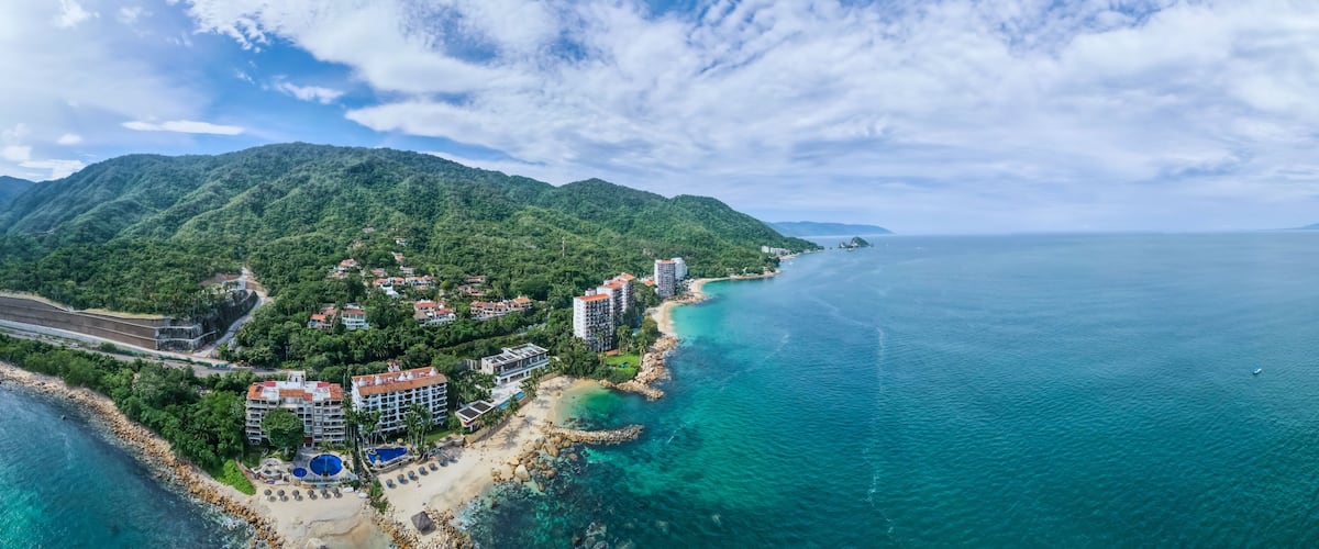 A coastal resort with a beach, clear turquoise waters, and a mountainous backdrop.