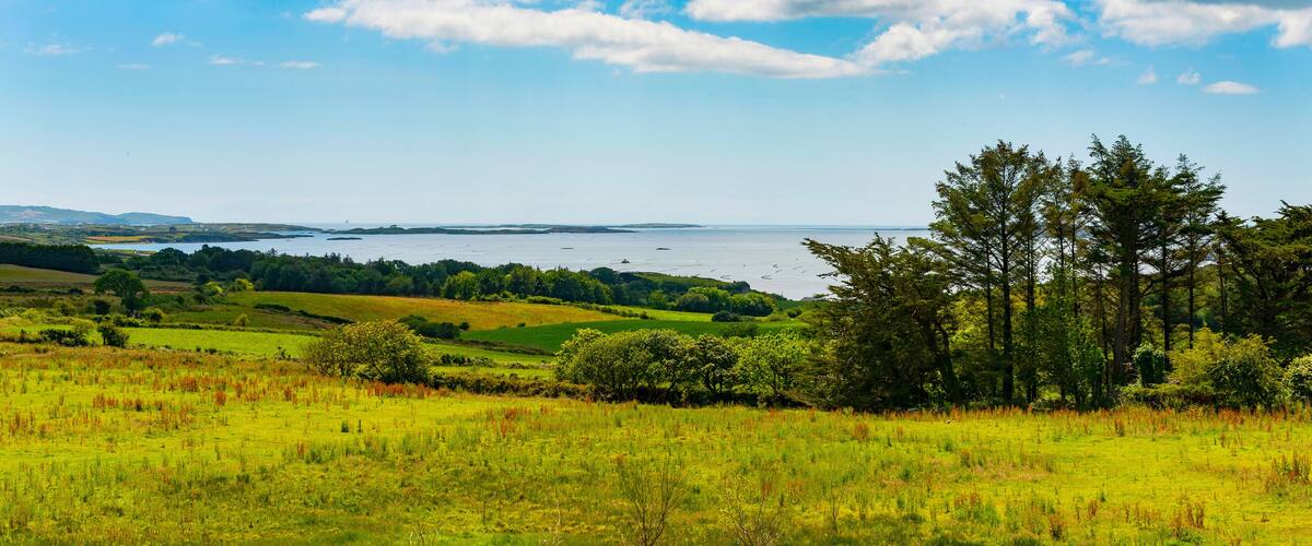 A coastal landscape with rolling hills, a body of water, and a clear sky.