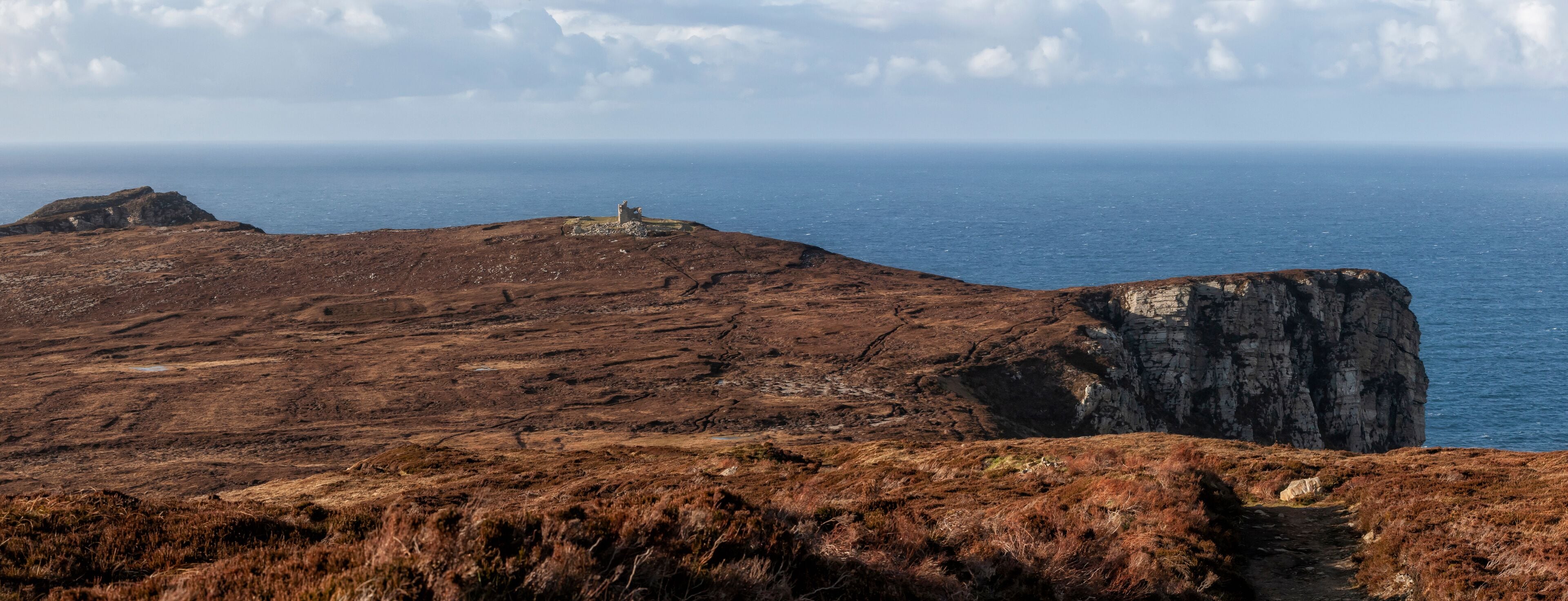 A rugged coastal landscape with a prominent cliff and a small structure on a hill.