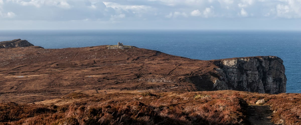 A rugged coastal landscape with a prominent cliff and a small structure on a hill.