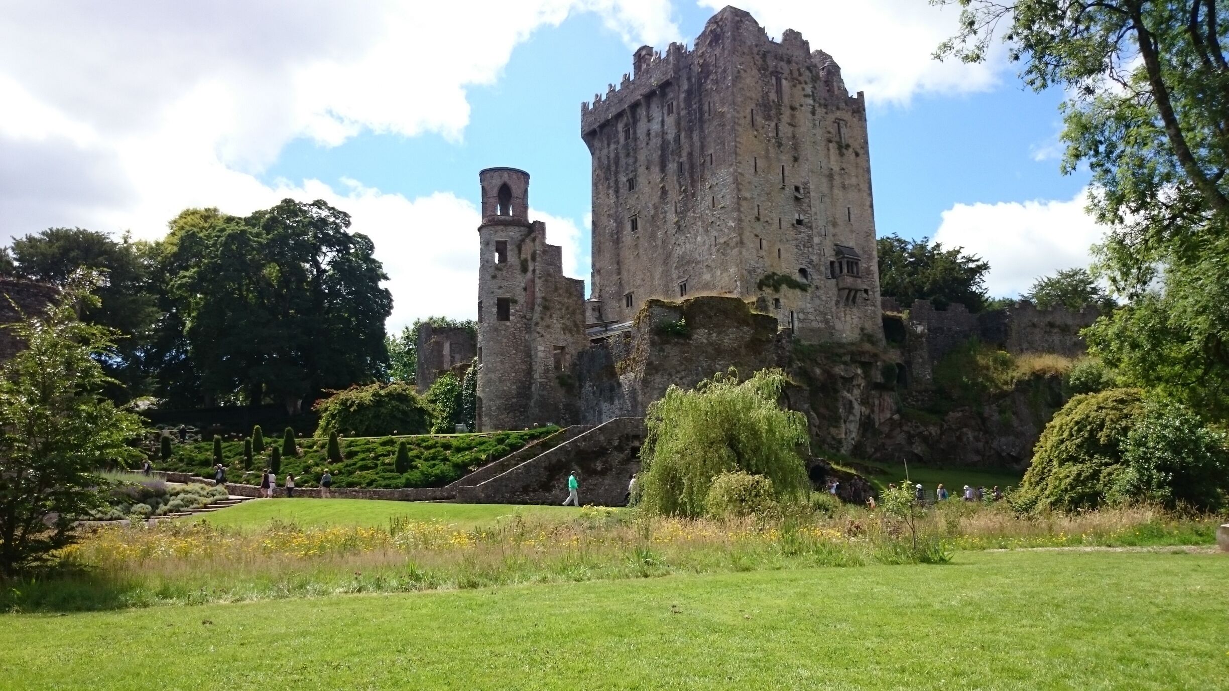 A historic castle with a large tower, surrounded by lush greenery and a well-maintained garden.