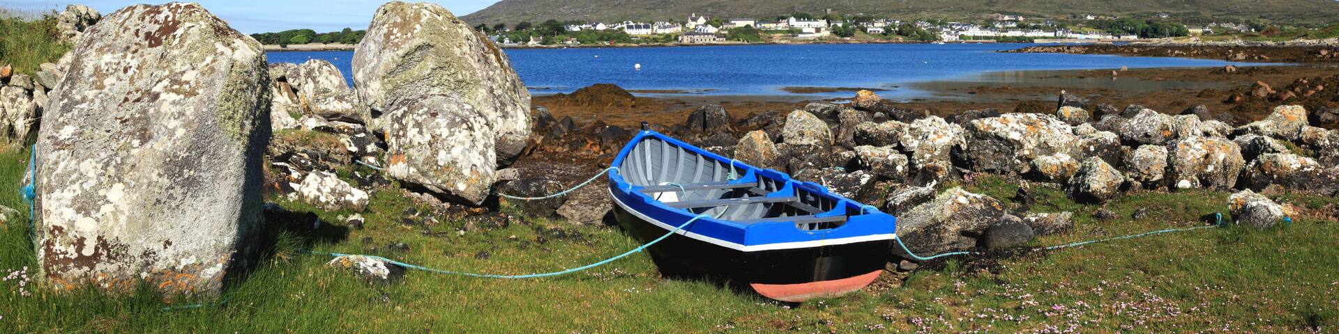 A Boat Tethered On Shore And A View Of Roundstone From Inishnee Island; County Galway, Ireland