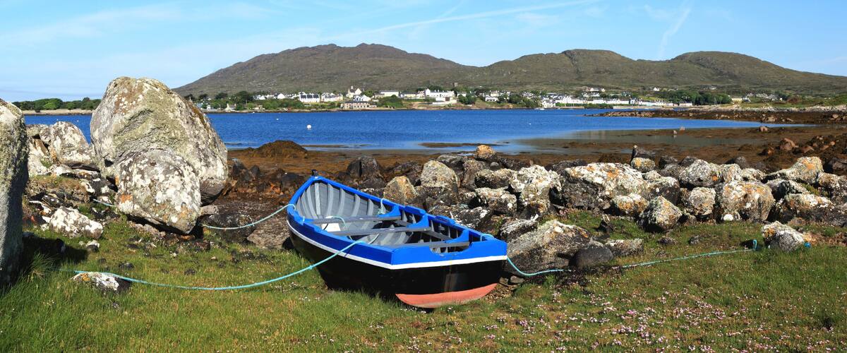 A small blue boat tied to a rock near a body of water with mountains in the background.