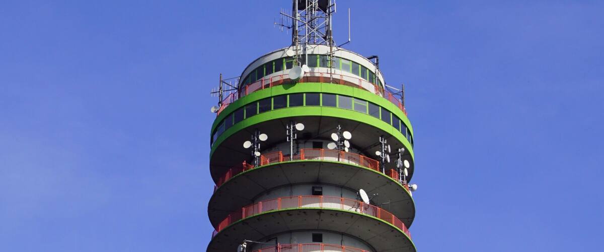 A tall, cylindrical tower with multiple balconies and a green and white color scheme, surrounded by trees.