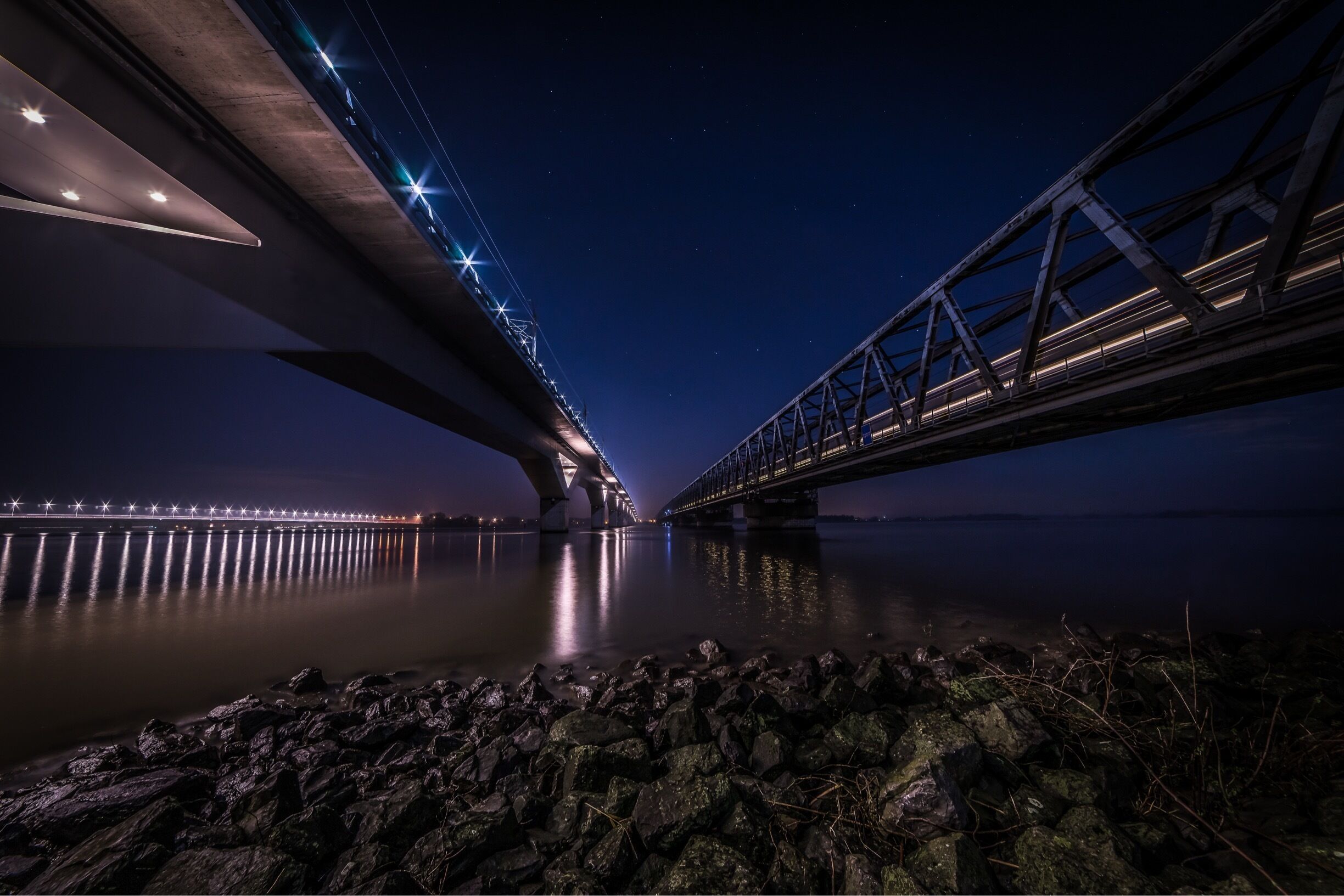 A nighttime view of a bridge with illuminated lights reflecting on the water.