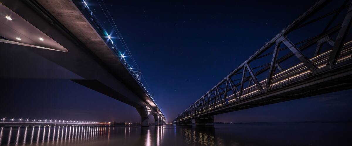A nighttime view of a bridge with illuminated lights reflecting on the water.