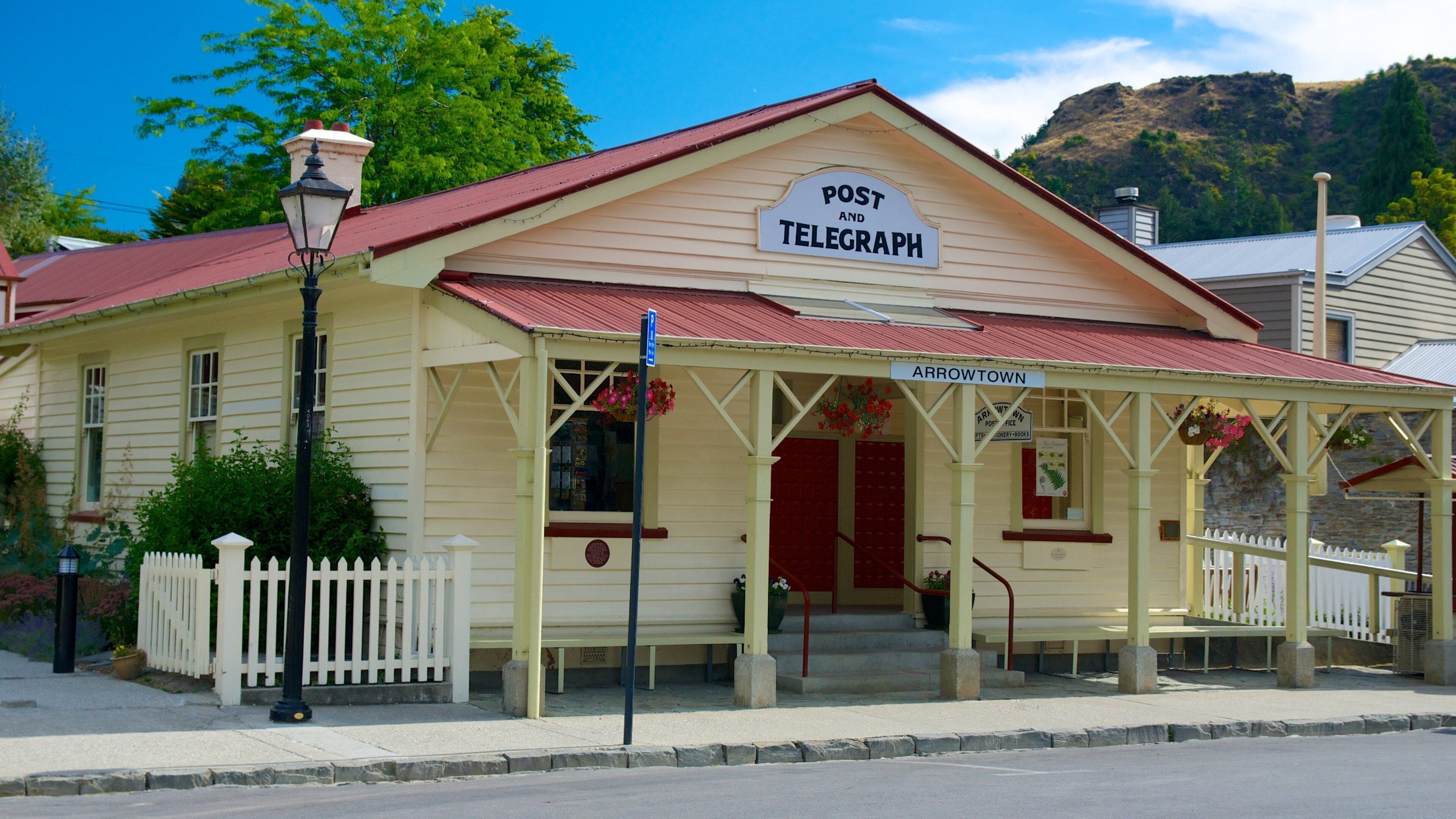 A vintage post and telegraph building with a red roof and a white picket fence.