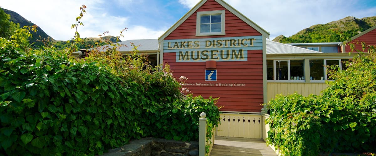 A red building labeled "Lakes District Museum" with a stone wall and greenery around it.