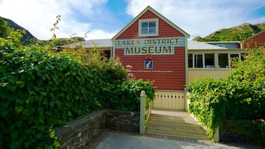 A red building labeled "Lakes District Museum" with a stone wall and greenery around it.