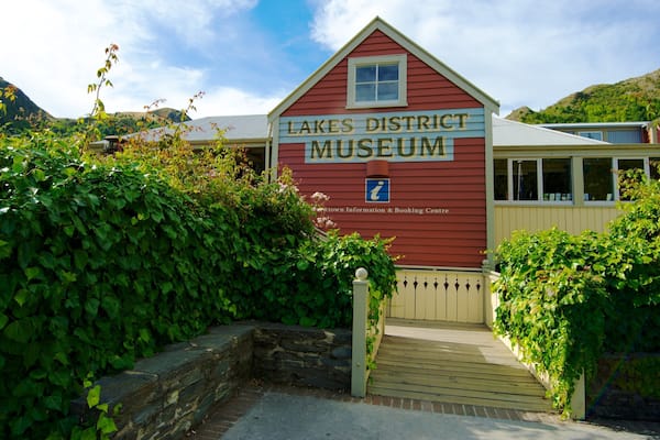 A red building labeled "Lakes District Museum" with a stone wall and greenery around it.