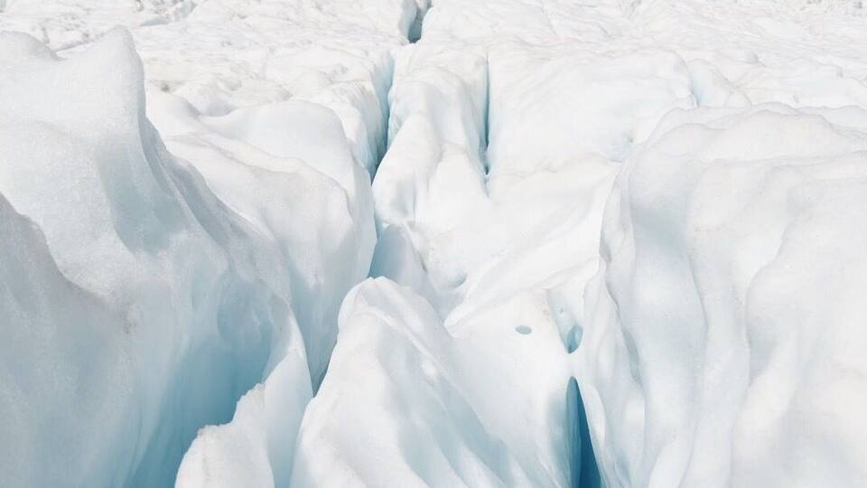 A glacier with crevasses and a mountainous background.