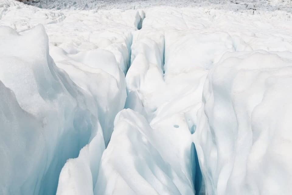 Un glacier parsemé de crevasses, avec une chaîne de montagnes en arrière-plan.