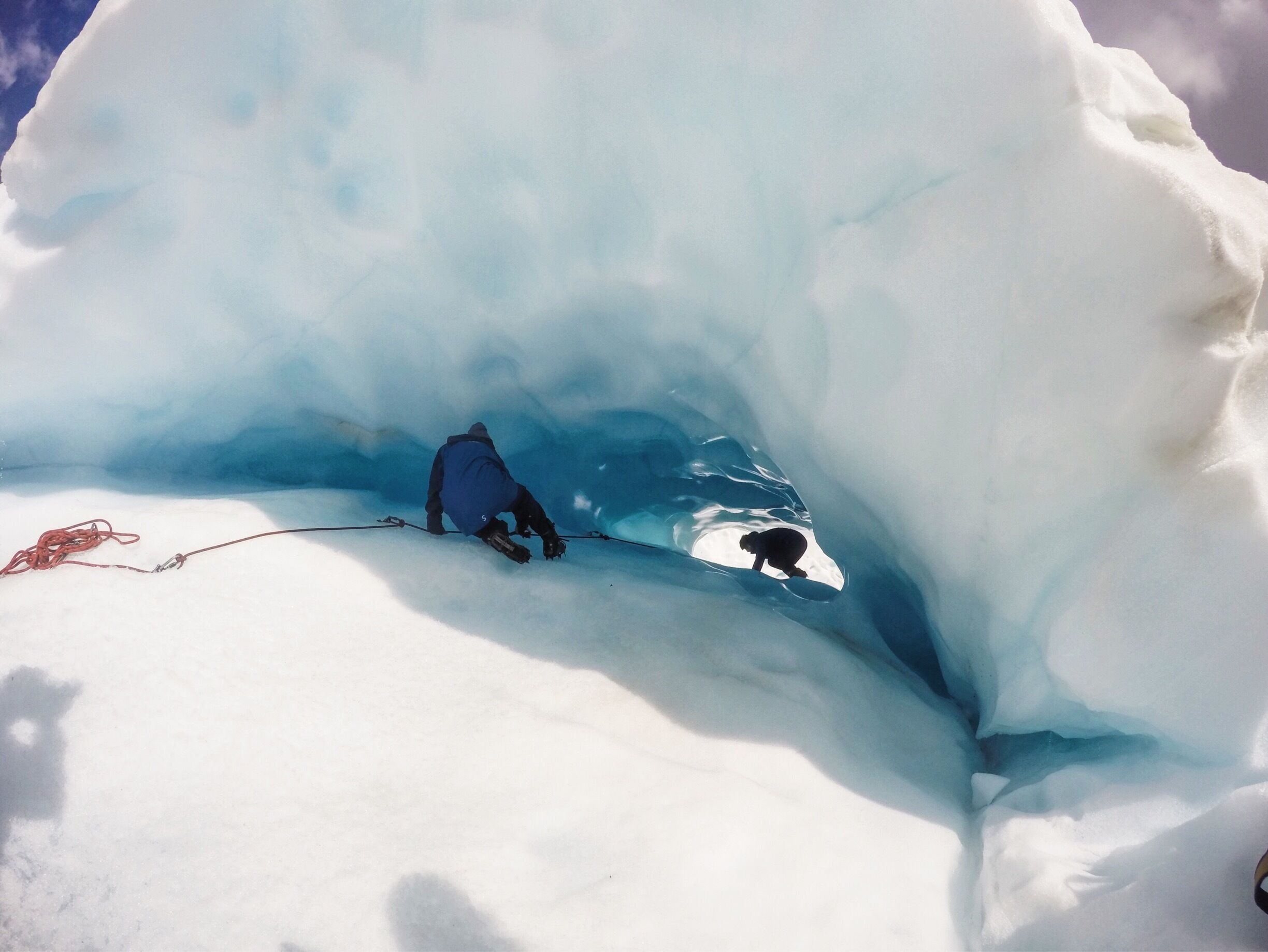 A person inside an ice cave with a rope.
