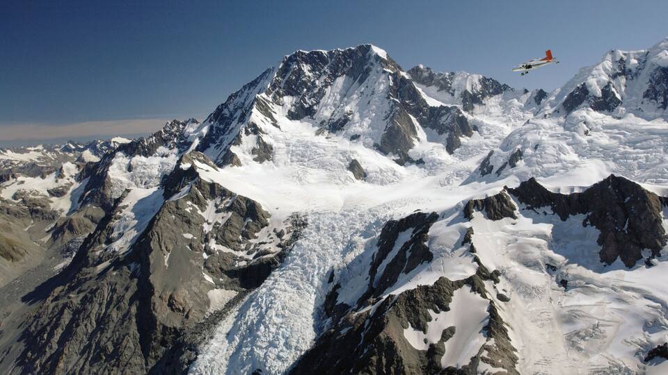 A snow-covered mountain range with a small airplane flying over.