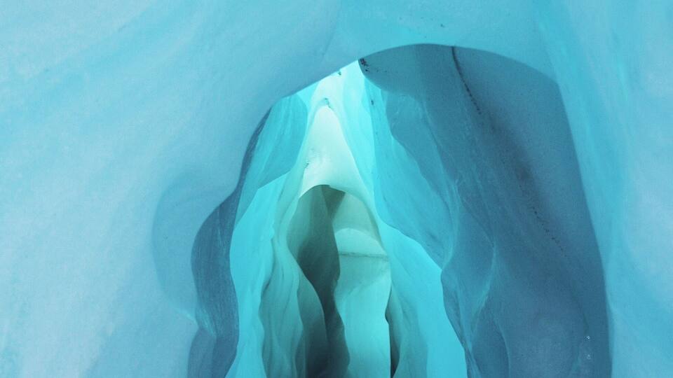 An ice cave with a narrow passage and a light source at the end.