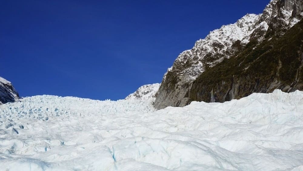 A group of people hiking on a snow-covered glacier with a clear blue sky.