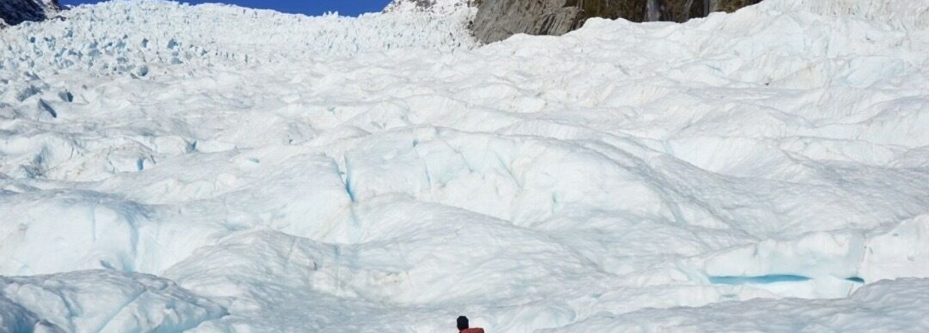 Um grupo de pessoas caminhando em uma geleira coberta de neve sob um céu azul e límpido.