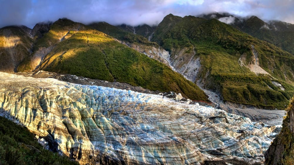 A glacier with steep, rocky cliffs and lush green vegetation.