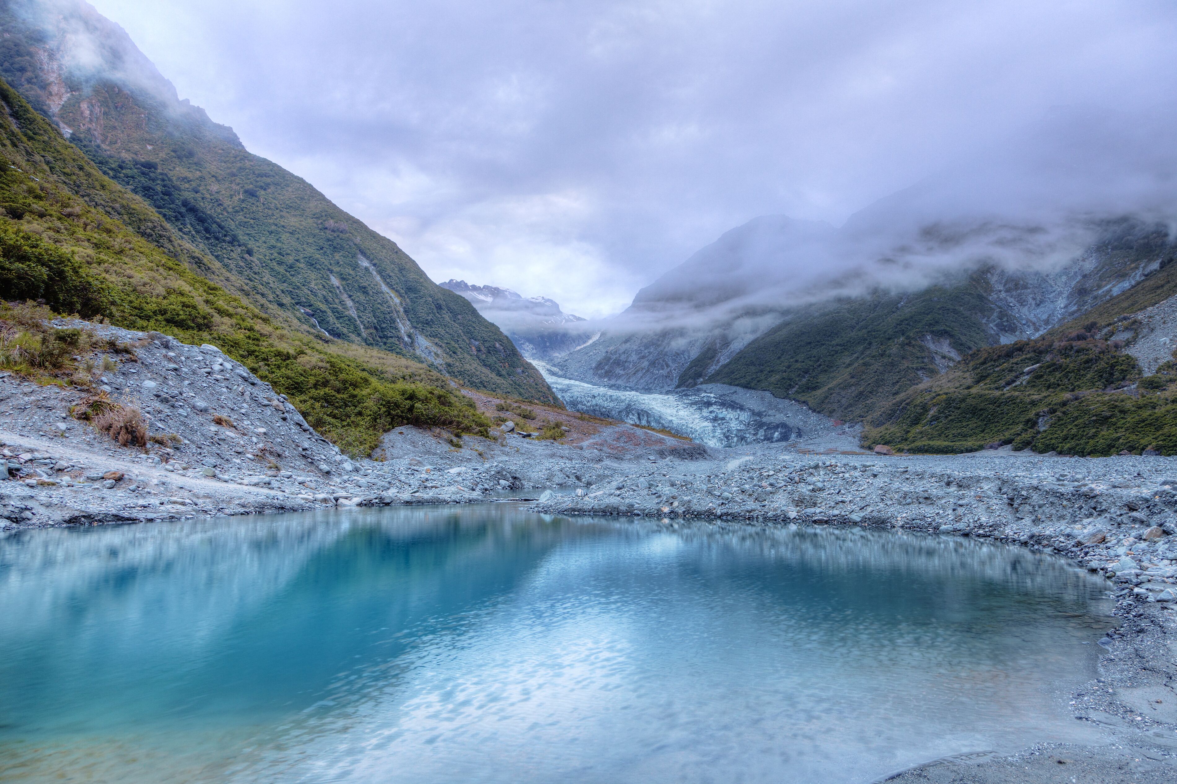 A glacier-fed lake surrounded by steep, forested mountains.