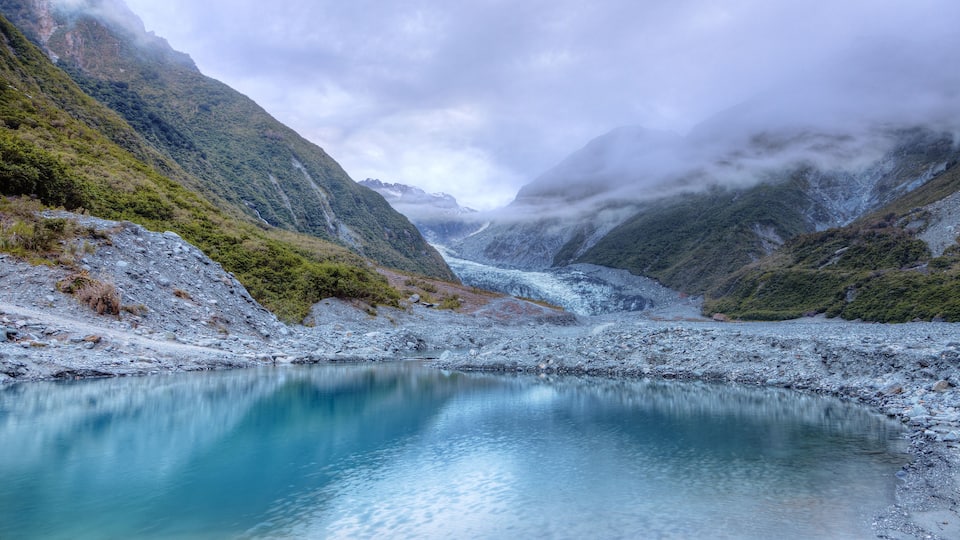A glacier-fed lake surrounded by steep, forested mountains.