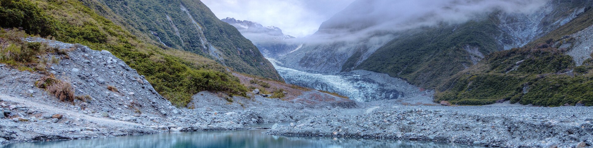 Un lago alimentado por un glaciar, rodeado de montañas escarpadas y boscosas.