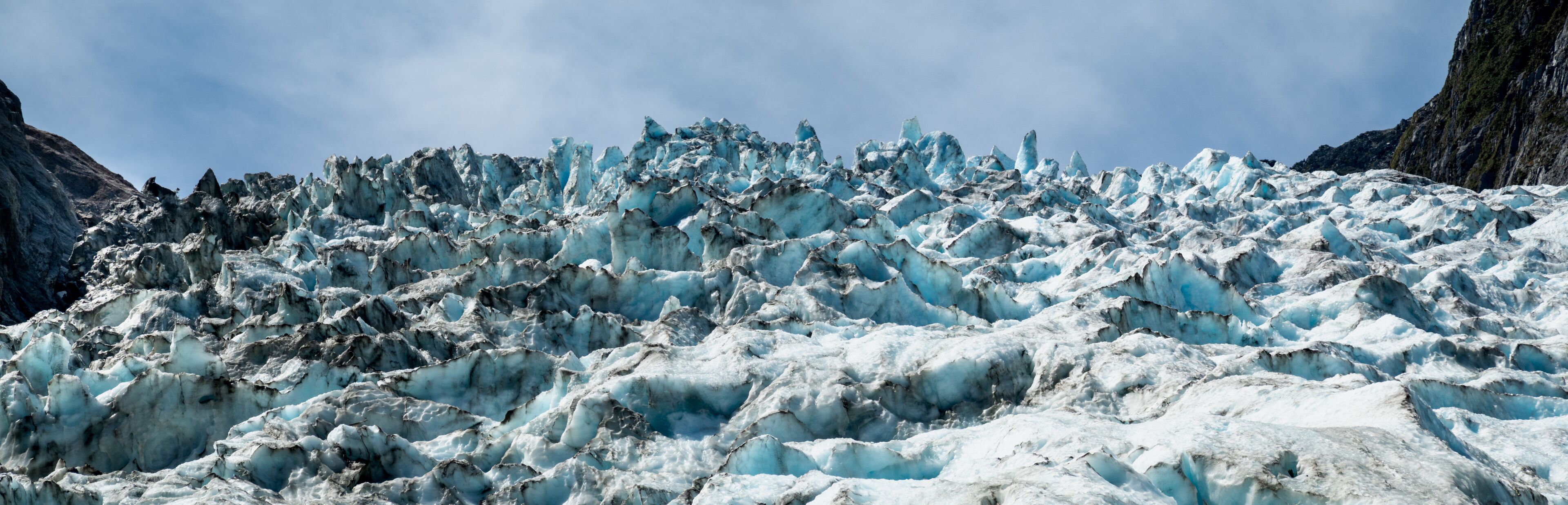 A glacier with rugged, jagged ice formations and steep rocky cliffs.