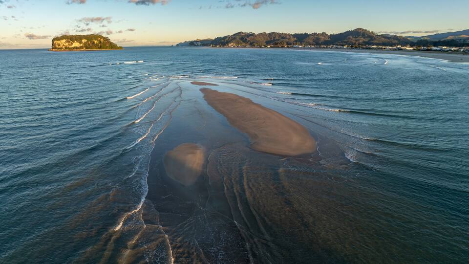 A coastal landscape with a beach, waves, and a distant island.