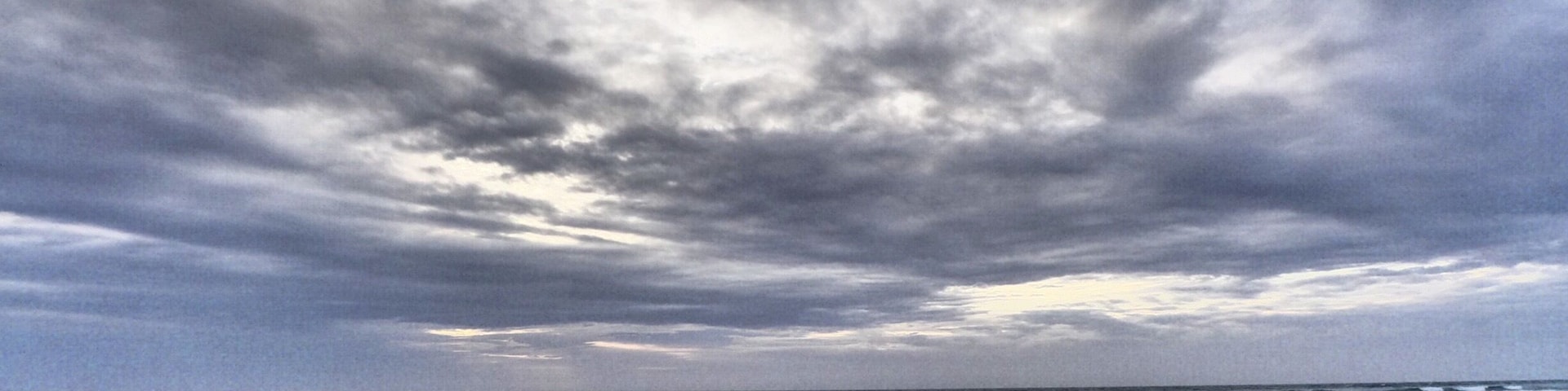 A beach with two people walking on the shore under a cloudy sky.