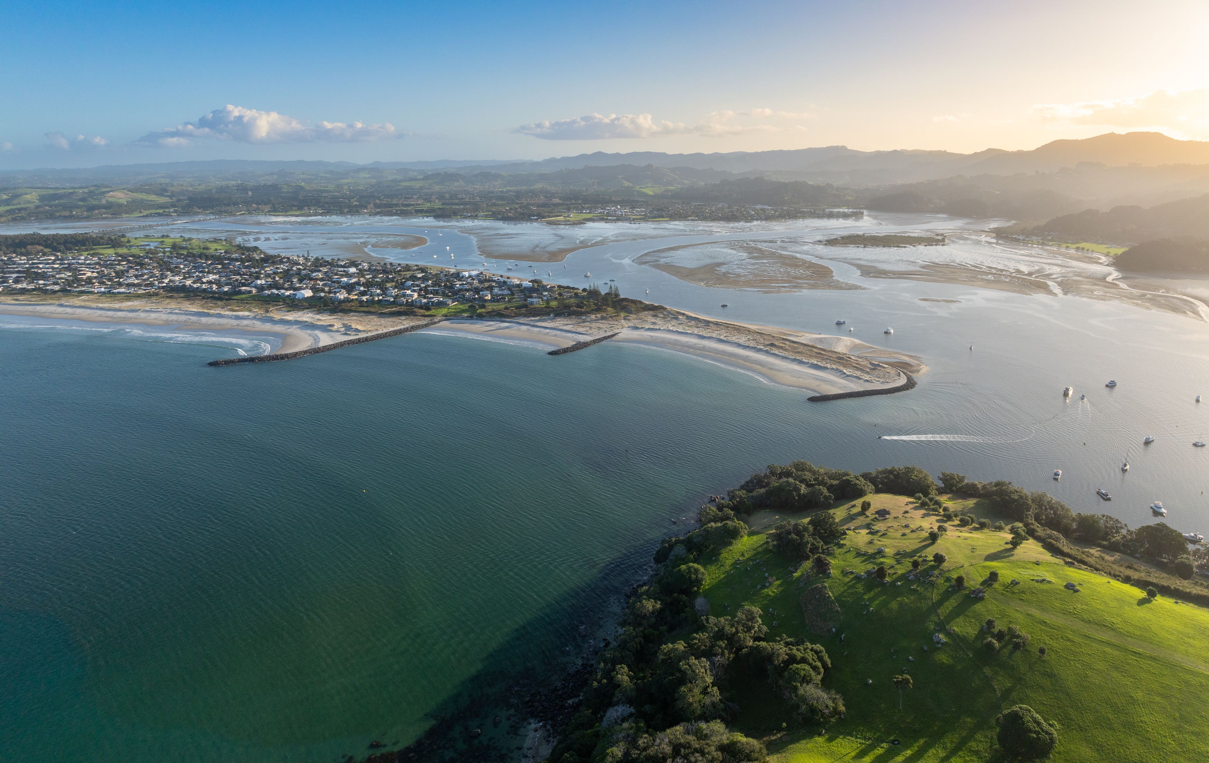 An aerial view of a coastal town with a marina, sandy beaches, and rolling hills in the background.