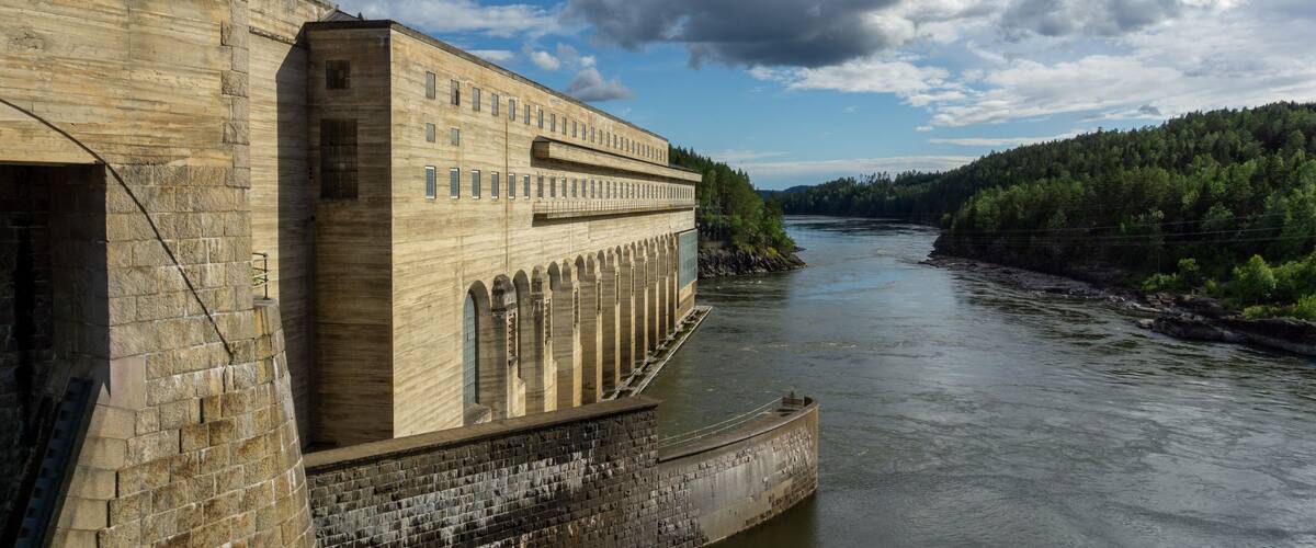 A large dam with multiple gates and a river flowing through a forested area.