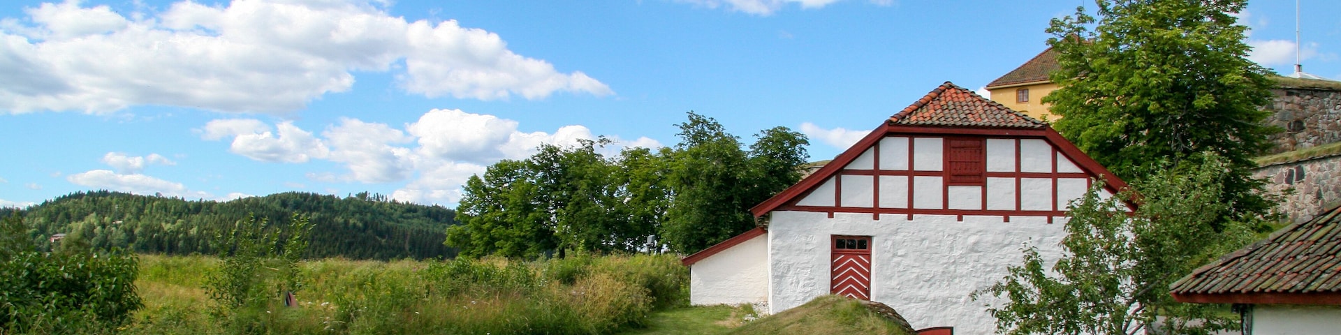 Una casa tradicional con entramado de madera, con puerta roja y paredes blancas, rodeada por un campo cubierto de césped y árboles.