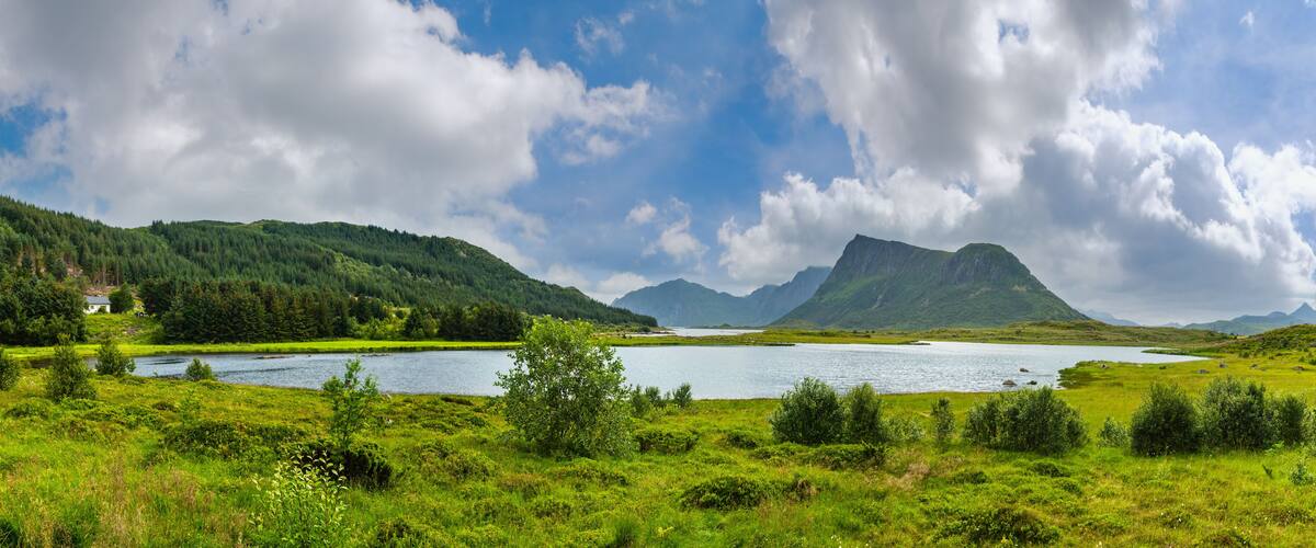 A lake surrounded by lush green hills and mountains under a partly cloudy sky.